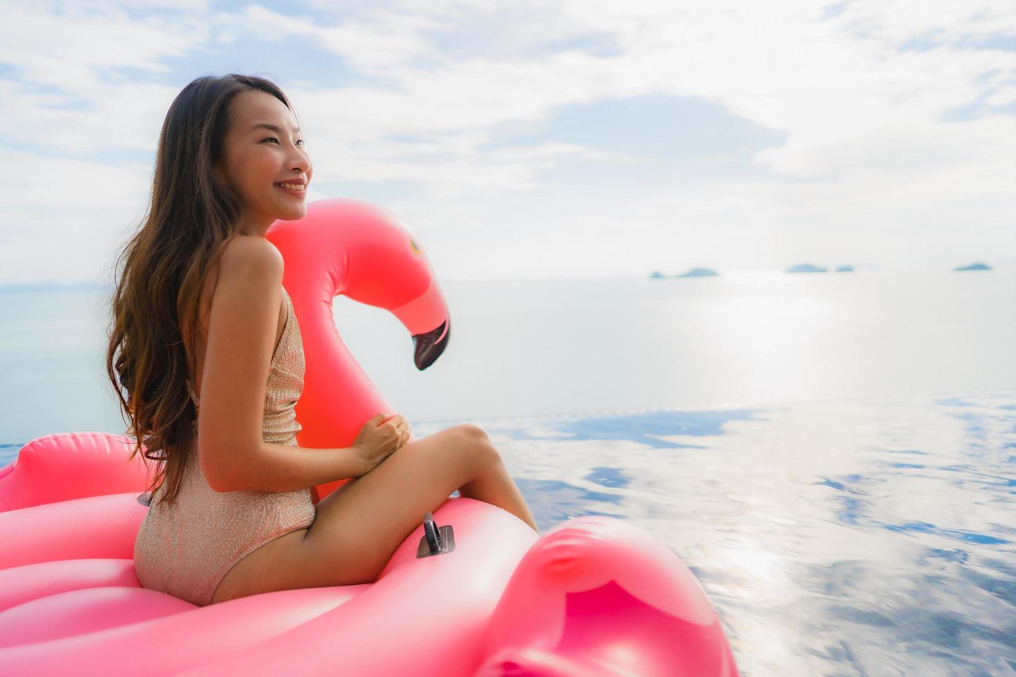 Ritratto di giovane donna asiatica sul fenicottero galleggiante gonfiabile intorno alla piscina all'aperto in hotel resort foto