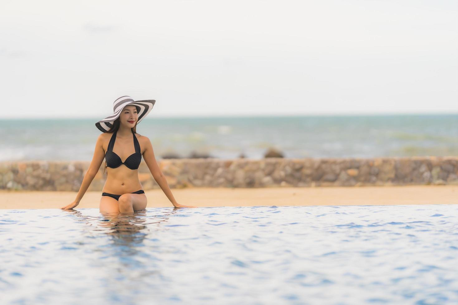 ritratto bella giovane donna asiatica indossare bikini intorno alla piscina in hotel resort quasi mare oceano spiaggia foto