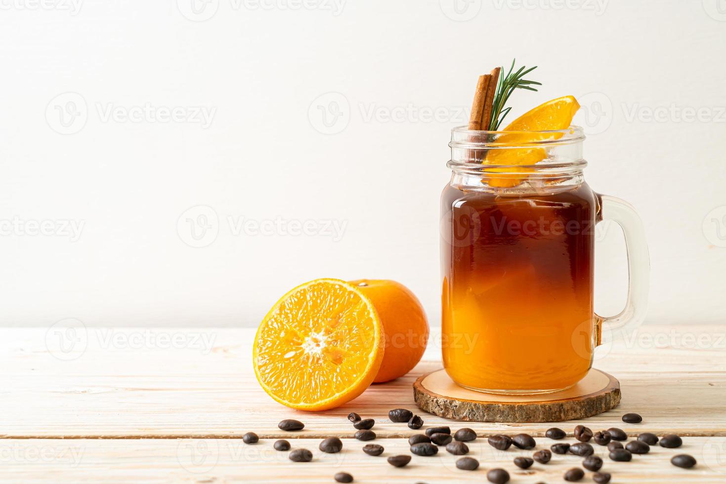 un bicchiere di caffè nero americano ghiacciato e uno strato di succo di arancia e limone decorato con rosmarino e cannella su uno sfondo di legno foto