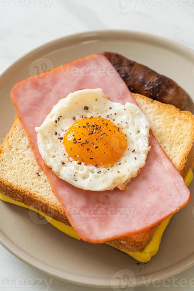 pane fatto in casa formaggio tostato, prosciutto cotto e uovo fritto con salsiccia di maiale a colazione foto