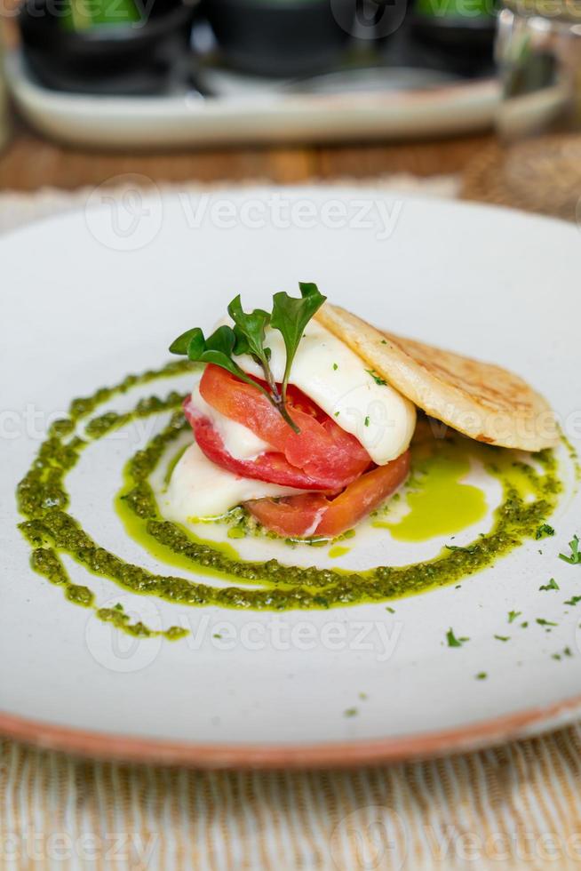 pomodoro con formaggio cheddar, pane tostato e salsa al pesto sul piatto - stile alimentare vegano e vegetale foto