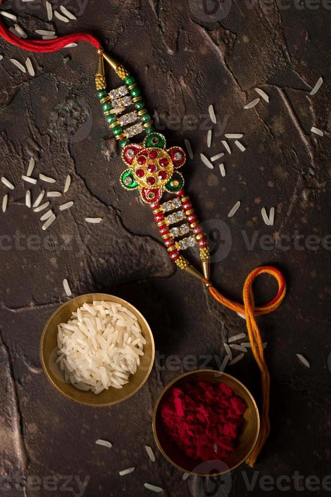 sfondo raksha bandhan con un elegante rakhi, chicchi di riso e kumkum. un tradizionale cinturino da polso indiano che è un simbolo di amore tra fratelli e sorelle. foto