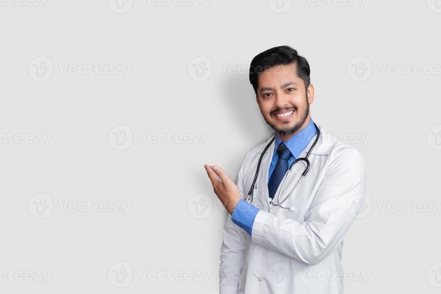 medico che indossa l'uniforme sorridente mentre presenta e indica isolato con spazio di copia foto