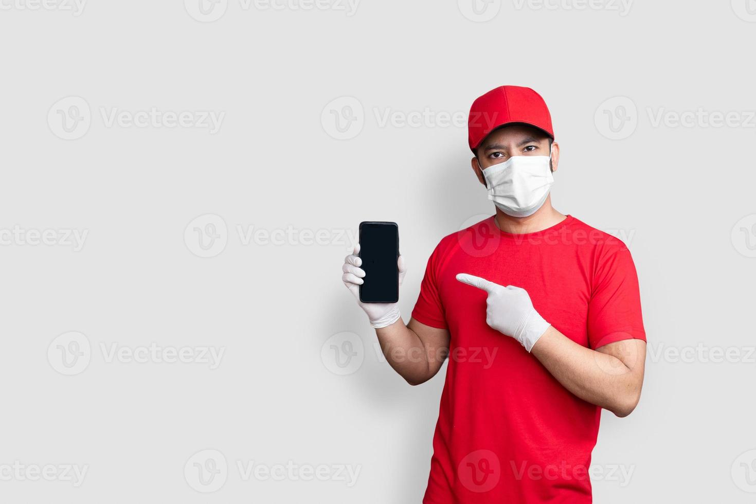 impiegato dell'addetto alle consegne con berretto rosso maglietta bianca uniforme maschera per il viso con applicazione di telefono cellulare nera isolata su sfondo bianco foto