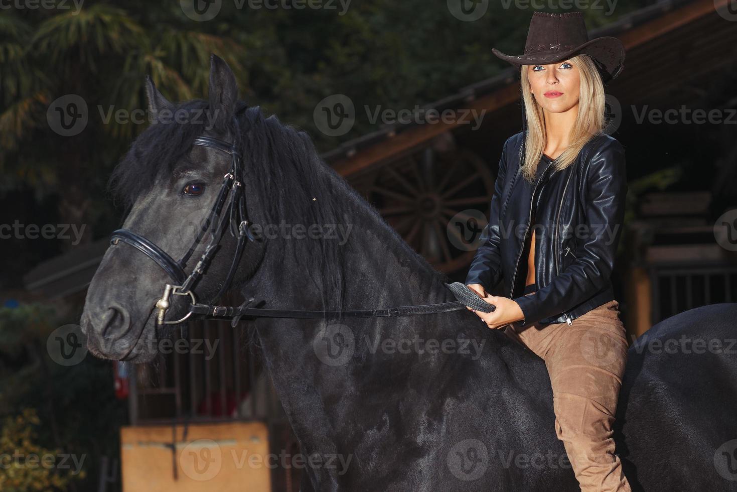 una bella ragazza bionda su un cavallo nero foto