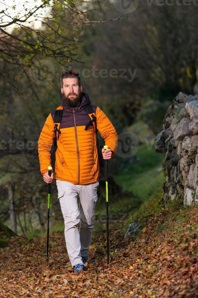 giovane con barba che pratica nordic walking nel sentiero delle foglie foto