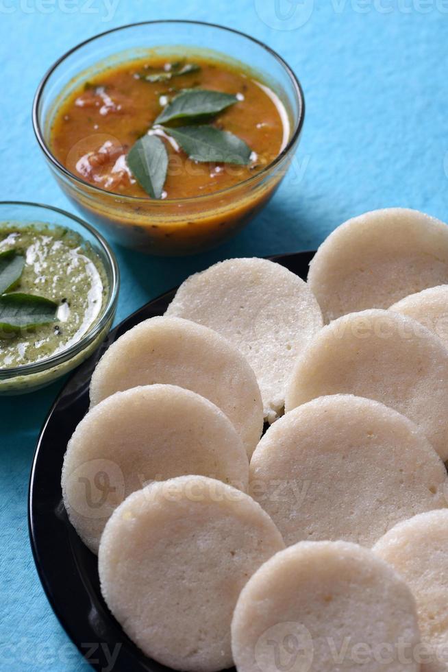 idli con sambar e chutney di cocco su sfondo blu, piatto indiano cibo preferito dell'India meridionale rava idli o semolino pigramente o rava pigramente, servito con sambar e chutney di cocco verde. foto