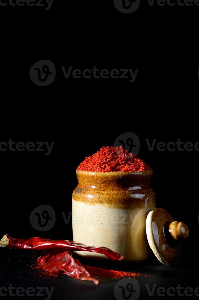 Peperoncino rosso in polvere in vaso di argilla con peperoncino rosso su sfondo nero foto