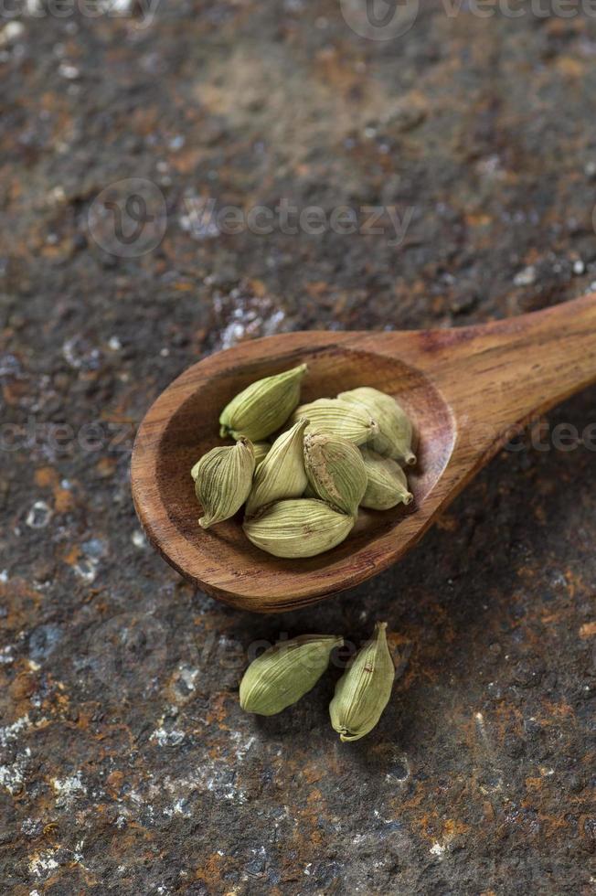 baccelli di cardamomo in cucchiaio di legno su uno sfondo strutturato foto