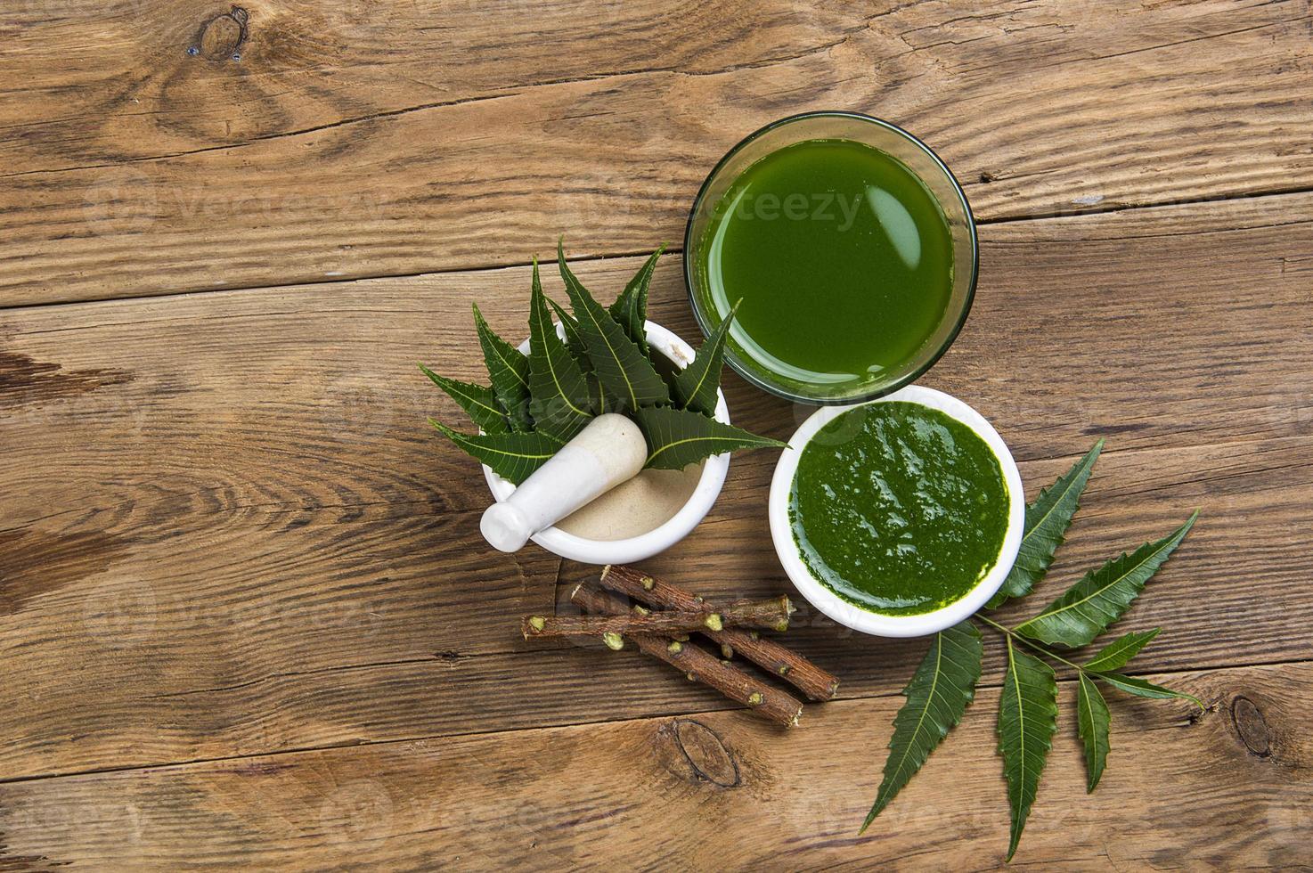 foglie medicinali di neem in mortaio e pestello con pasta di neem, succo e ramoscelli su fondo di legno foto