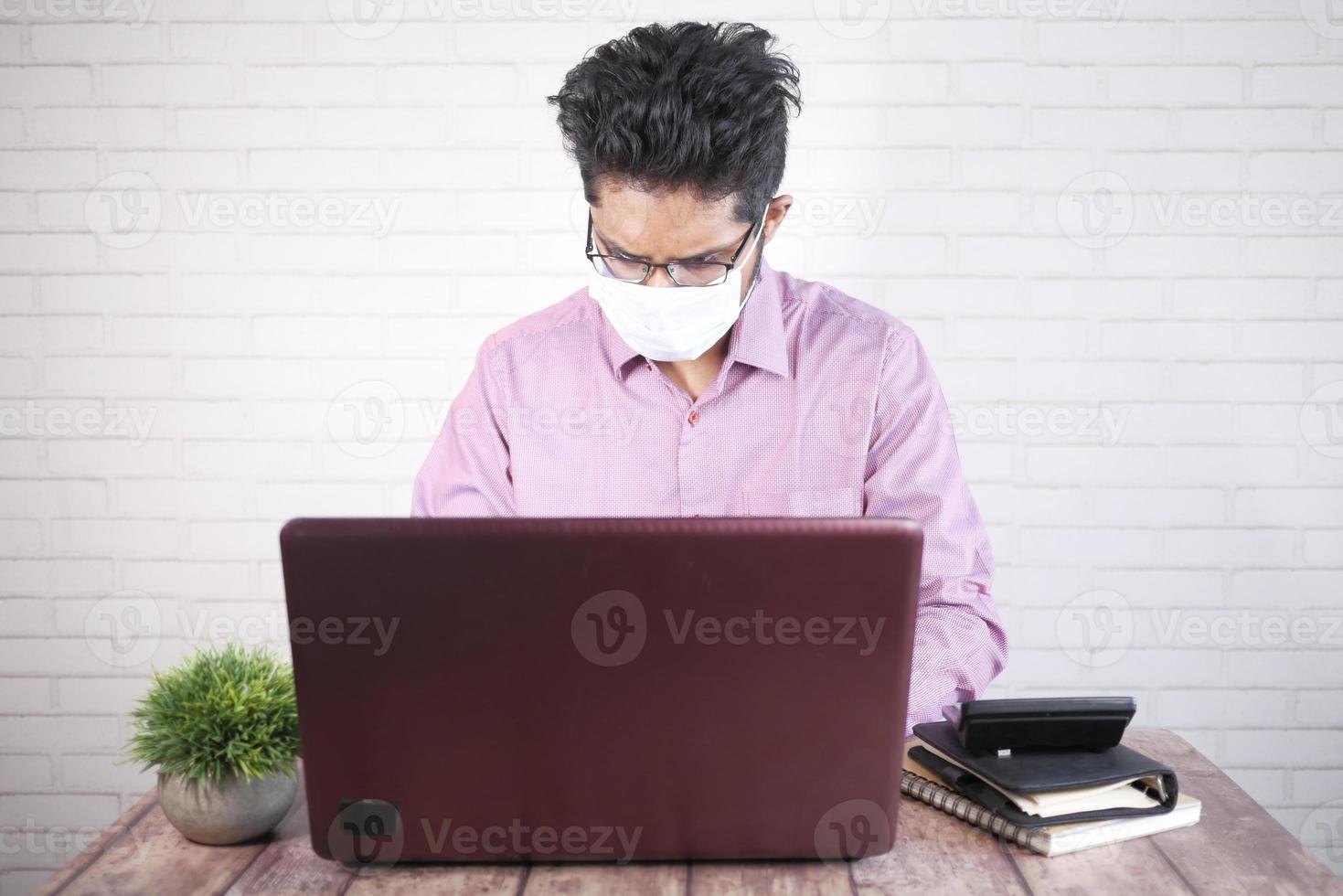 uomo d'affari in maschera facciale che lavora al computer portatile foto