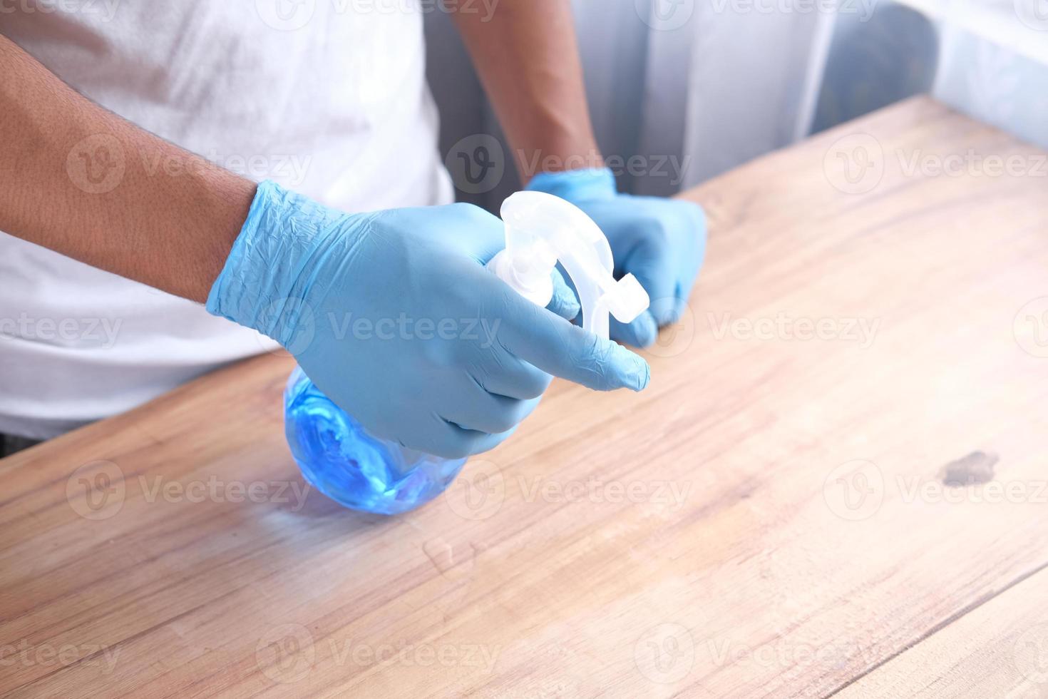 mano in guanti di gomma blu che tengono il tavolo per la pulizia della bottiglia spray foto
