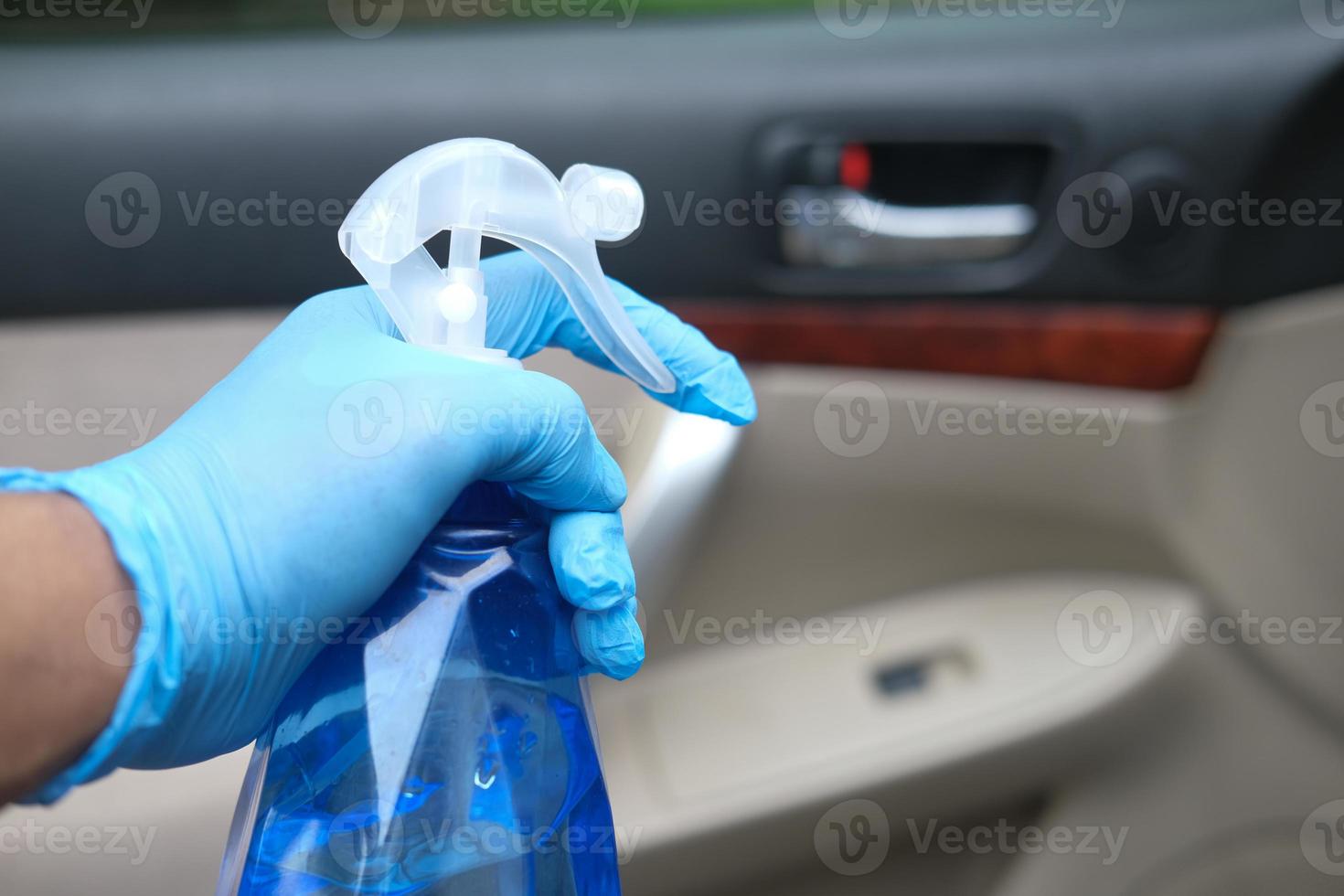 mano nei guanti che tengono la bottiglia spray per pulire la portiera dell'auto foto