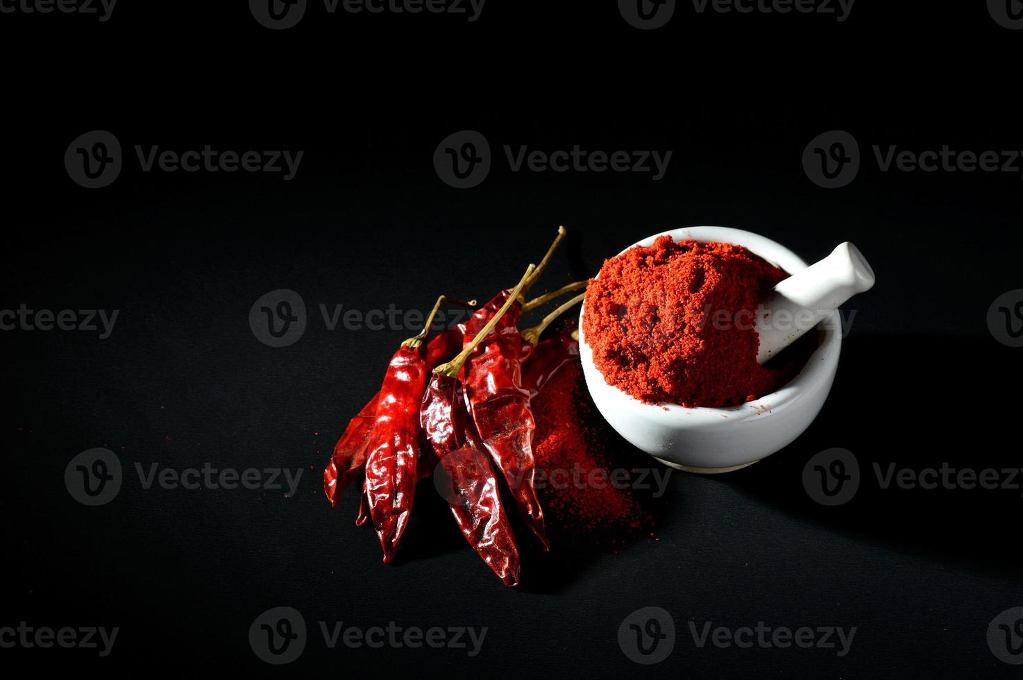 Peperoncino rosso in polvere in pestello con mortaio e peperoncino rosso su sfondo nero foto