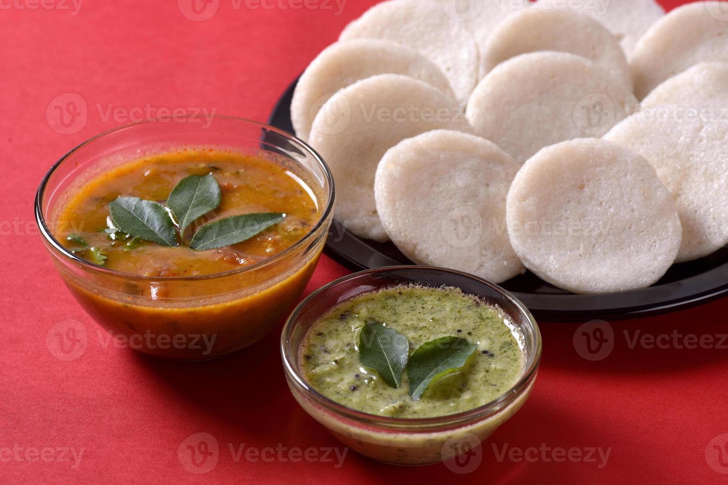 idli con sambar e chutney di cocco su sfondo rosso, piatto indiano cibo preferito dell'India meridionale rava idli o semolino pigramente o rava pigramente, servito con sambar e chutney verde. foto