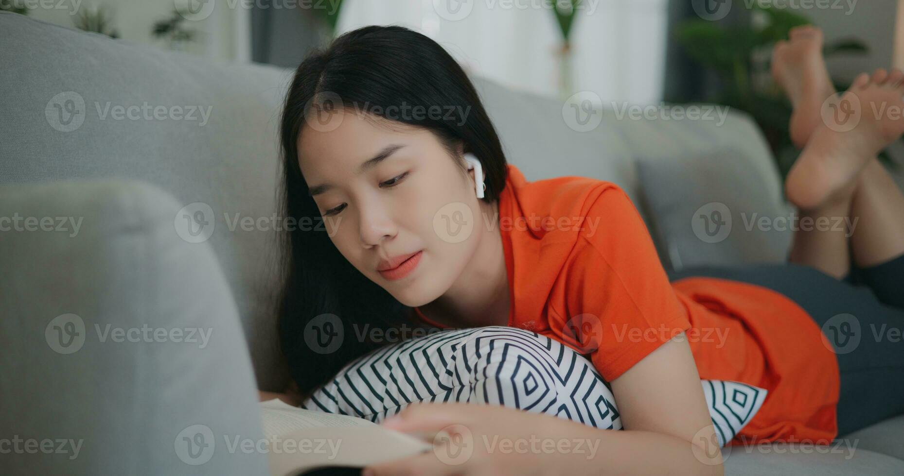 asiatico donna lettura un' libro mentre dire bugie su il divano foto