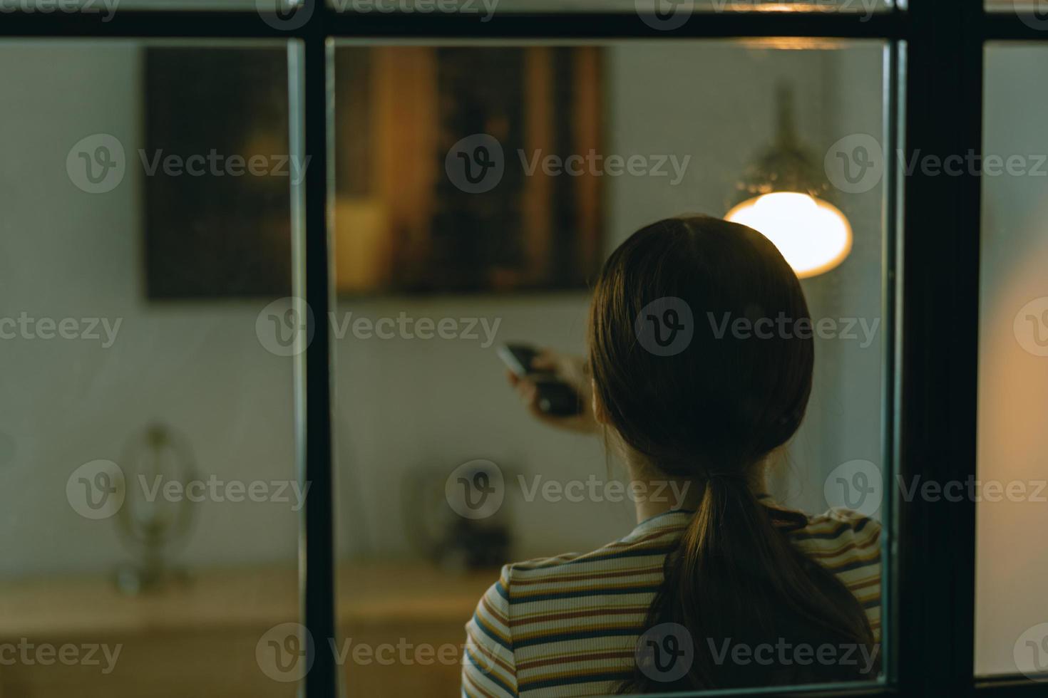 immagine sfocata di una donna asiatica seduta a guardare la televisione da sola sul divano di notte foto