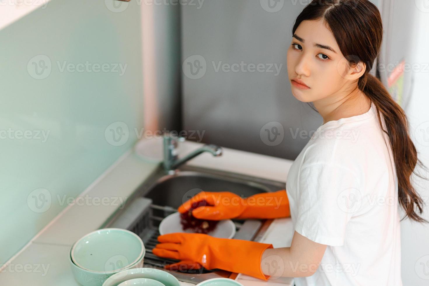 la donna asiatica sta lavando i piatti di umore stanco foto