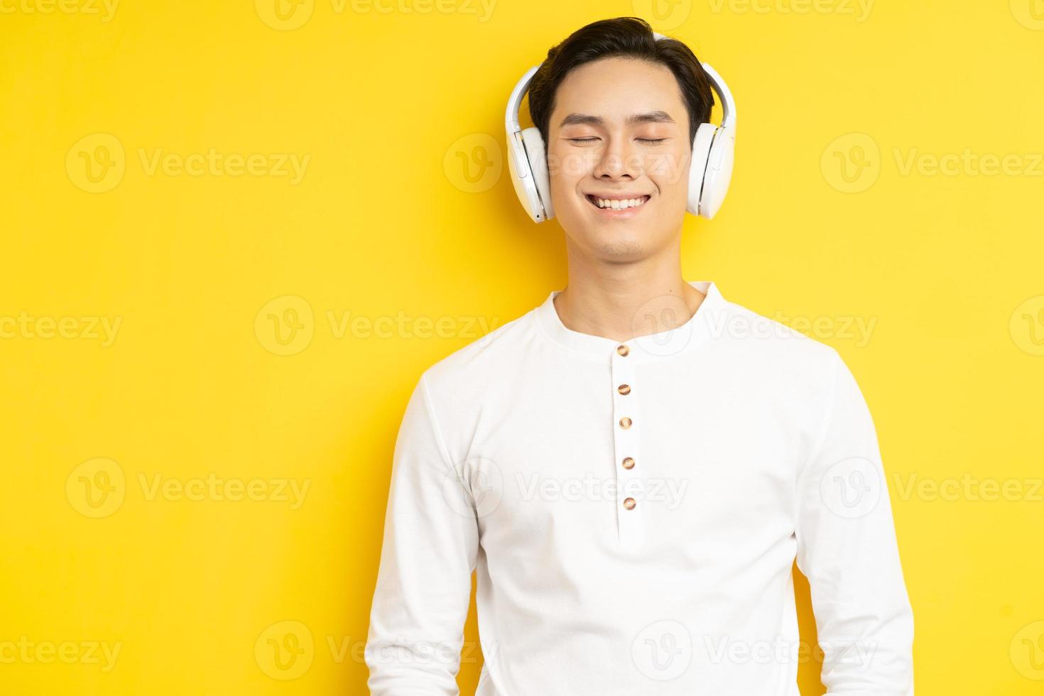 foto di un uomo asiatico in camicia bianca che ascolta musica con gli occhi chiusi su sfondo giallo