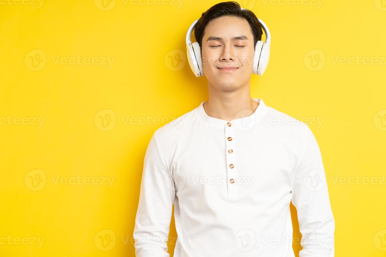 foto di un uomo asiatico in camicia bianca che ascolta musica con gli occhi chiusi su sfondo giallo