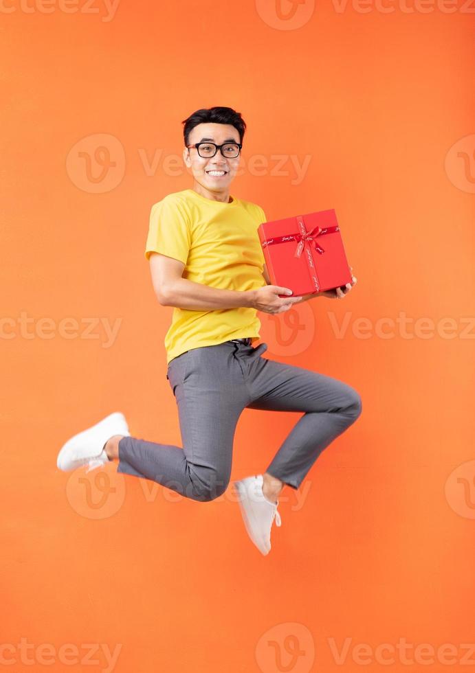 uomo asiatico in maglietta gialla che salta su sfondo arancione foto
