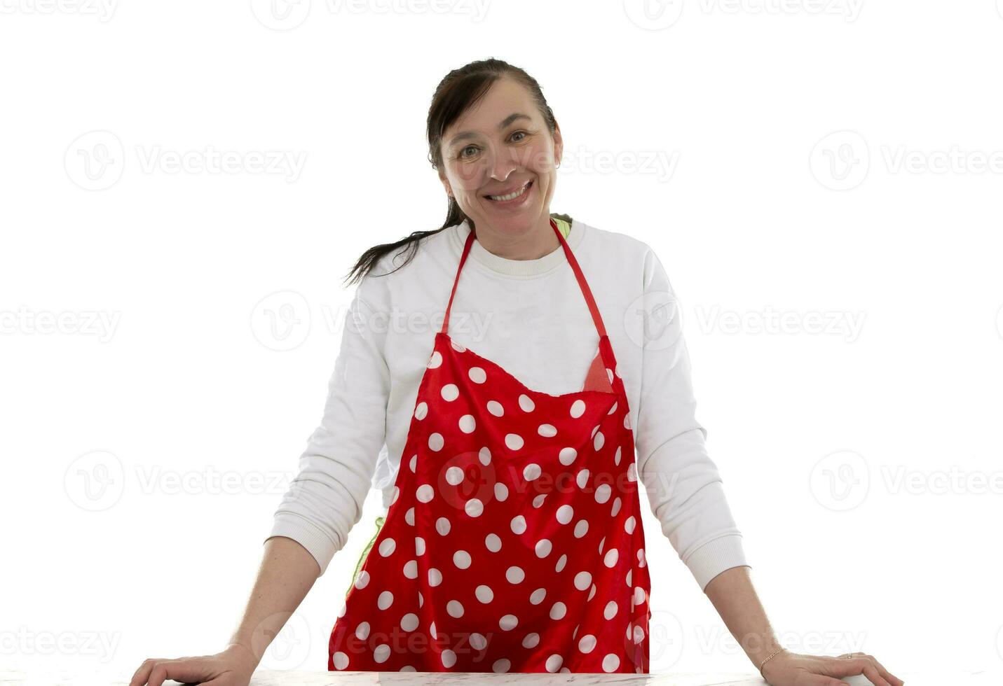 un' di mezza età donna nel un' culinario grembiule con rosso polka puntini su un' bianca sfondo. foto