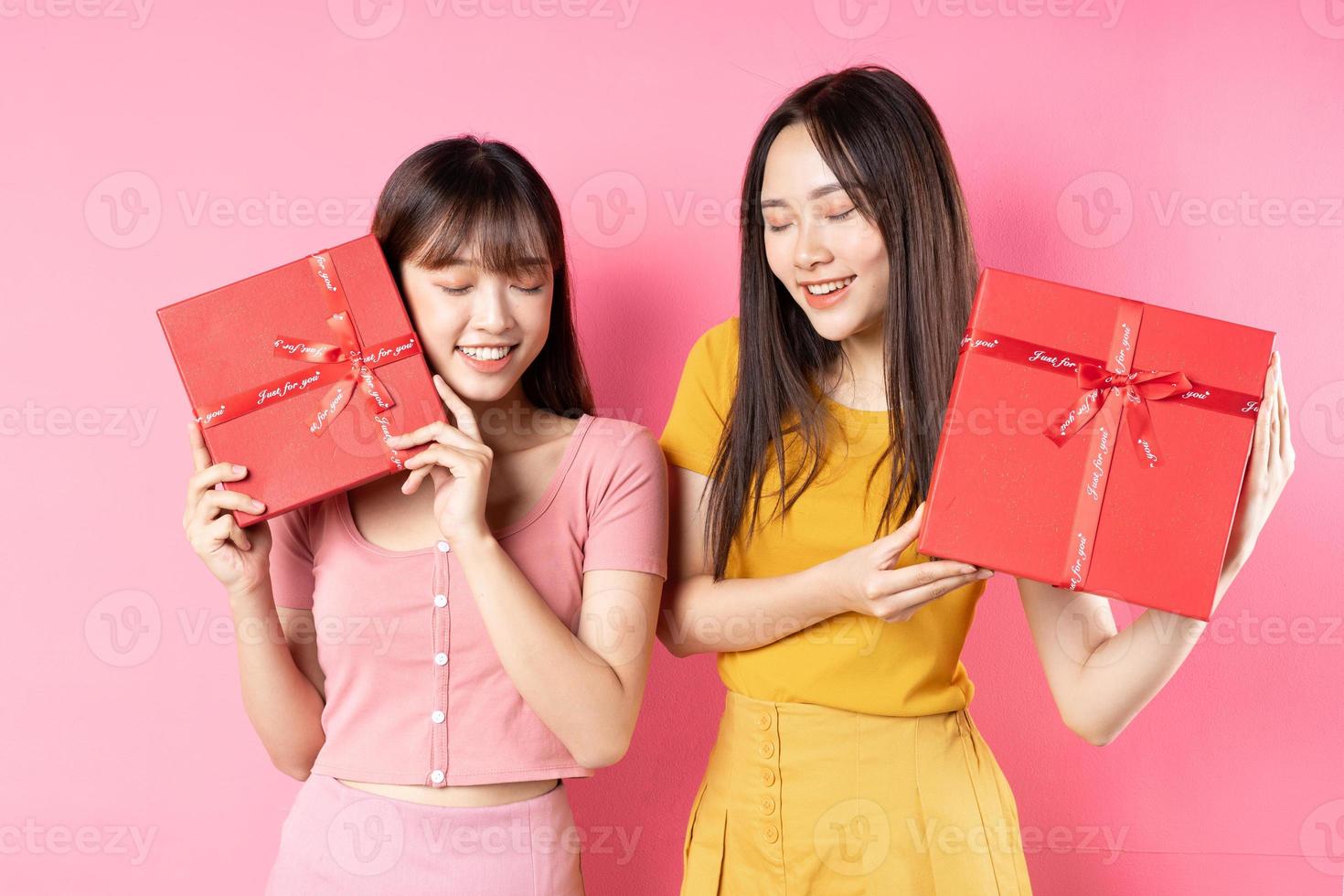 ritratto di due belle ragazze asiatiche che tengono una confezione regalo rossa su uno sfondo rosa foto