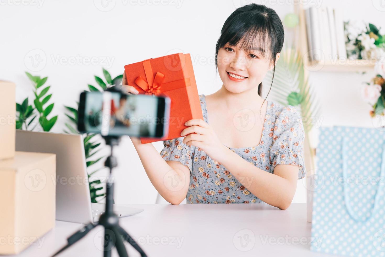 giovane donna asiatica in diretta streaming per fare regali al pubblico che guarda il suo streaming su piattaforme di social network foto