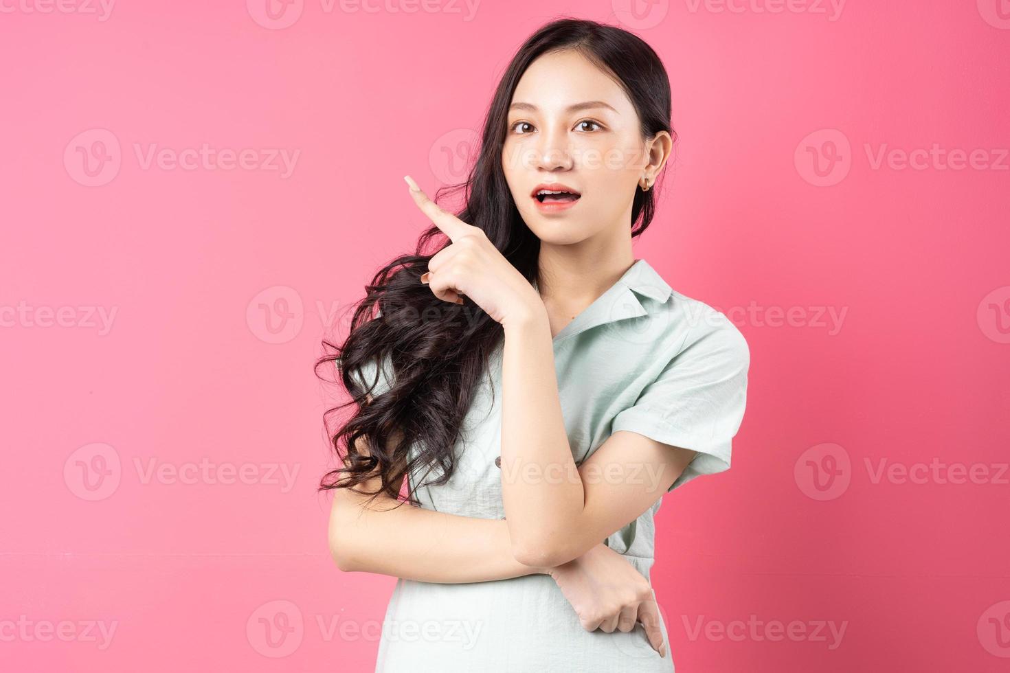 giovane donna asiatica che punta verso l'alto con il viso allegro foto