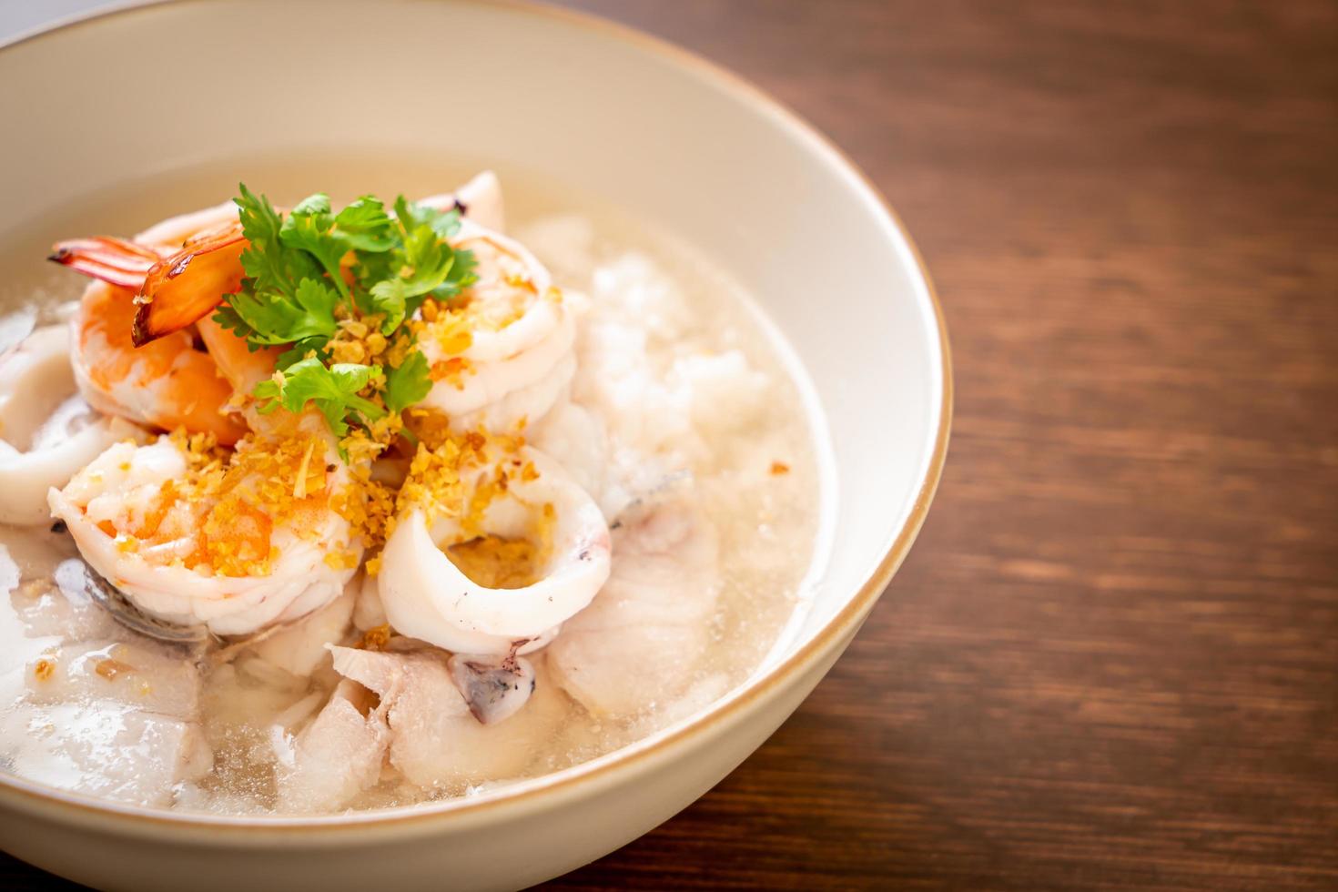 zuppa di porridge o riso bollito con frutti di mare di gamberi, calamari e pesce in una ciotola foto