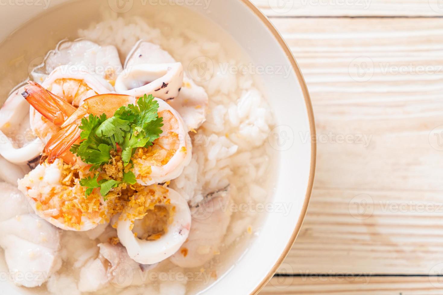 zuppa di porridge o riso bollito con frutti di mare di gamberi, calamari e pesce in una ciotola foto