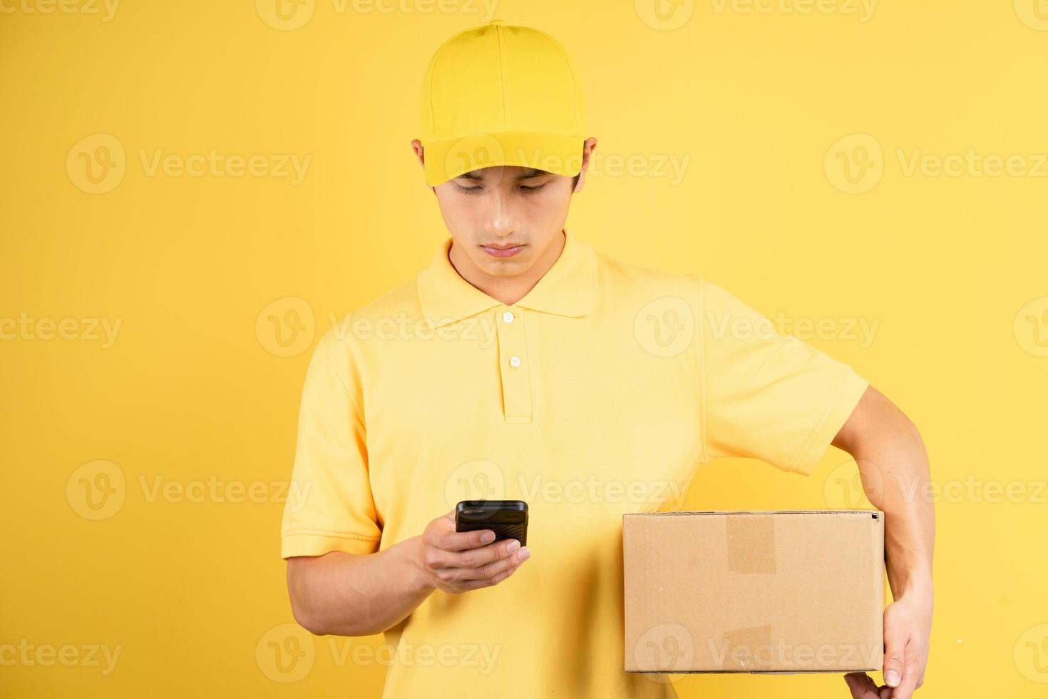 ritratto del maschio di consegna che tiene la scatola di carico e usa il telefono su sfondo giallo foto