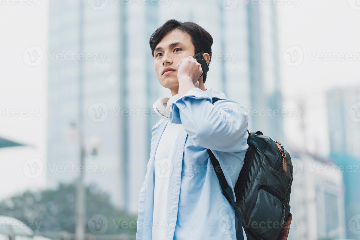 giovane uomo asiatico che indossa uno zaino ed è al telefono foto