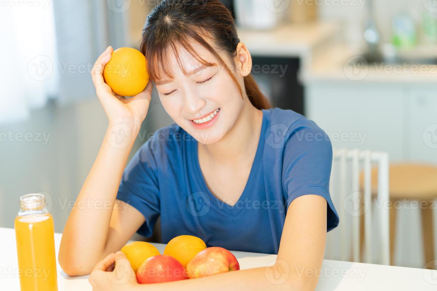una giovane donna asiatica che fa colazione con la frutta nella sua cucina foto