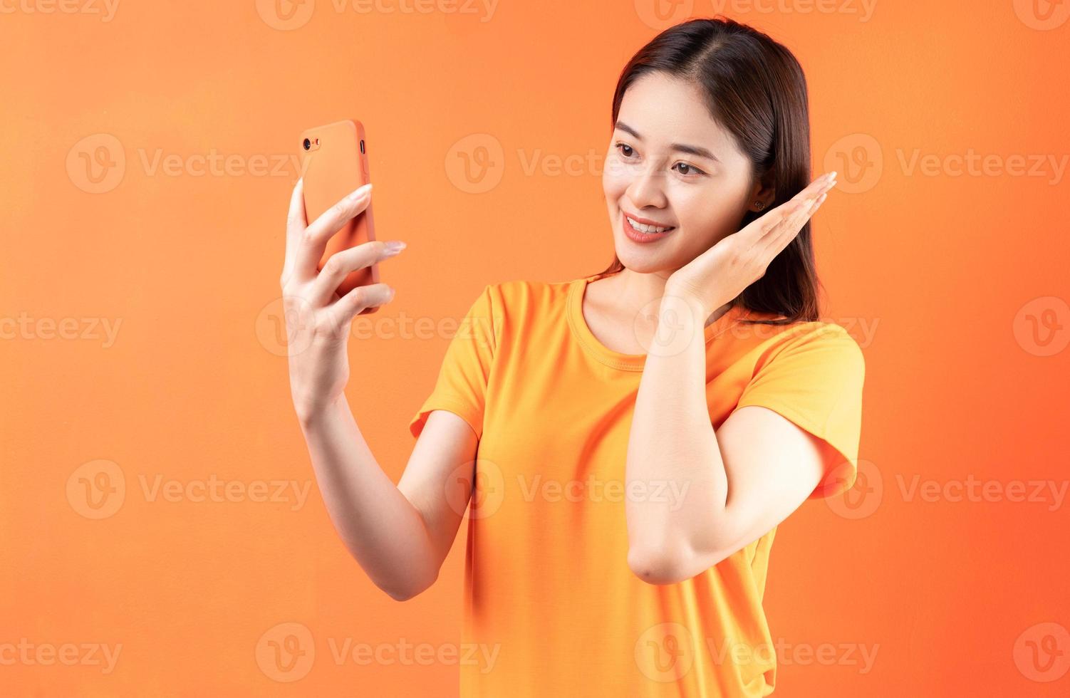 immagine di una giovane donna asiatica che tiene in mano uno smartphone su sfondo arancione foto
