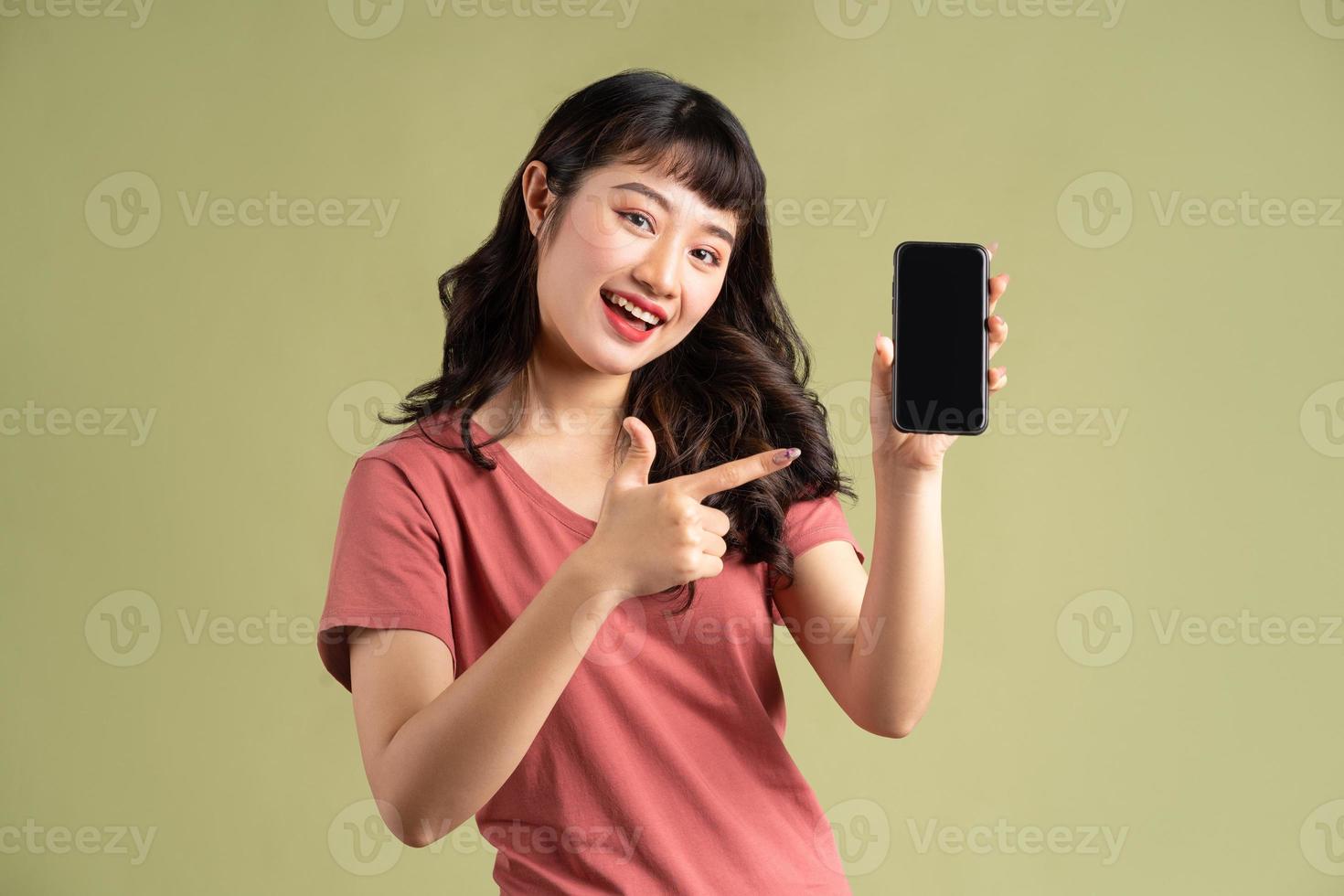 la donna asiatica sorridente punta il dito verso il telefono con uno schermo vuoto foto
