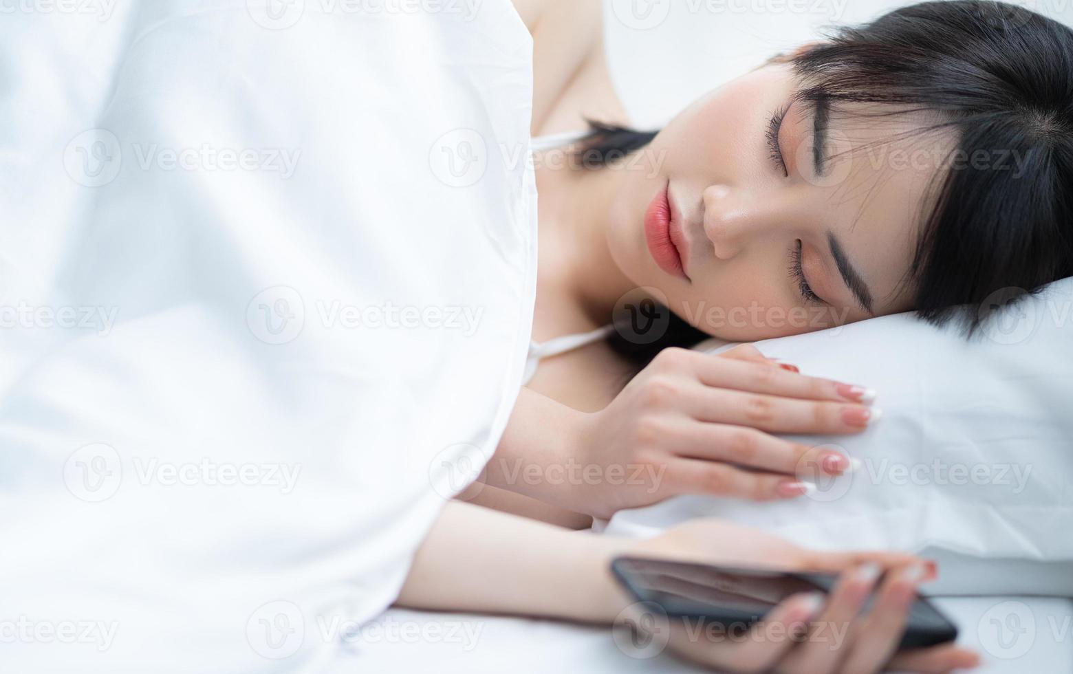 bella donna asiatica che usa il telefono sul letto in camera da letto foto