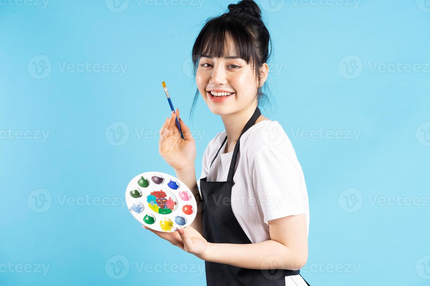 bella pittrice asiatica che tiene in mano una penna d'oca e una tavolozza di colori su sfondo blu foto