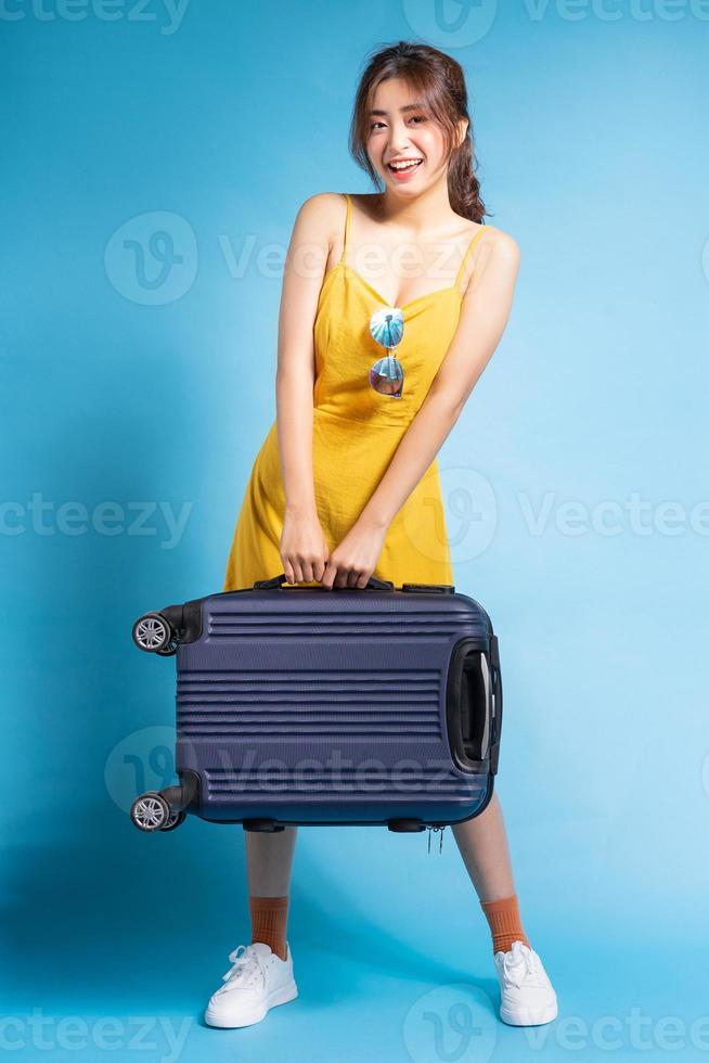 giovane donna asiatica che tiene la valigia su sfondo blu, concetto estivo foto