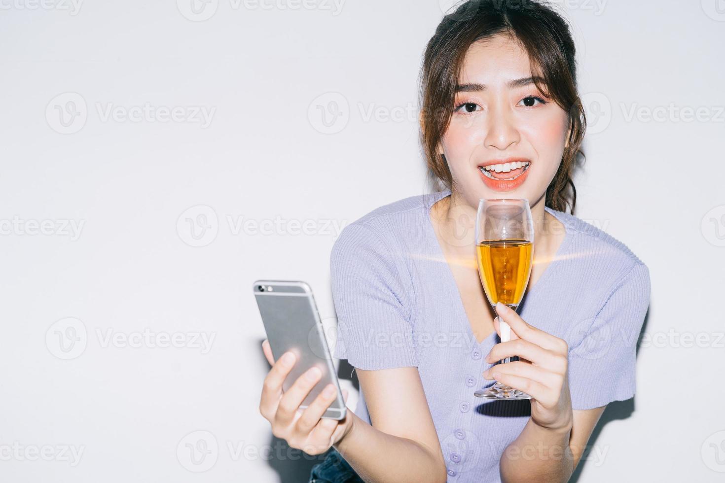 giovane donna asiatica che beve vino e utilizza lo smartphone su sfondo bianco foto