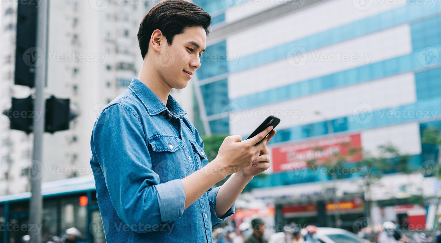 giovane uomo asiatico che cammina e usa lo smartphone per strada foto