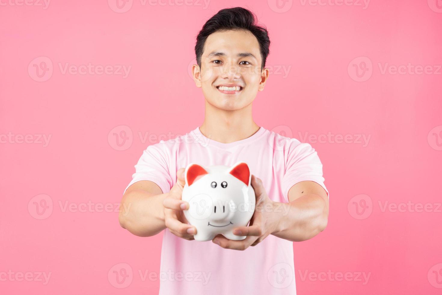 giovane uomo asiatico che tiene salvadanaio su sfondo rosa foto