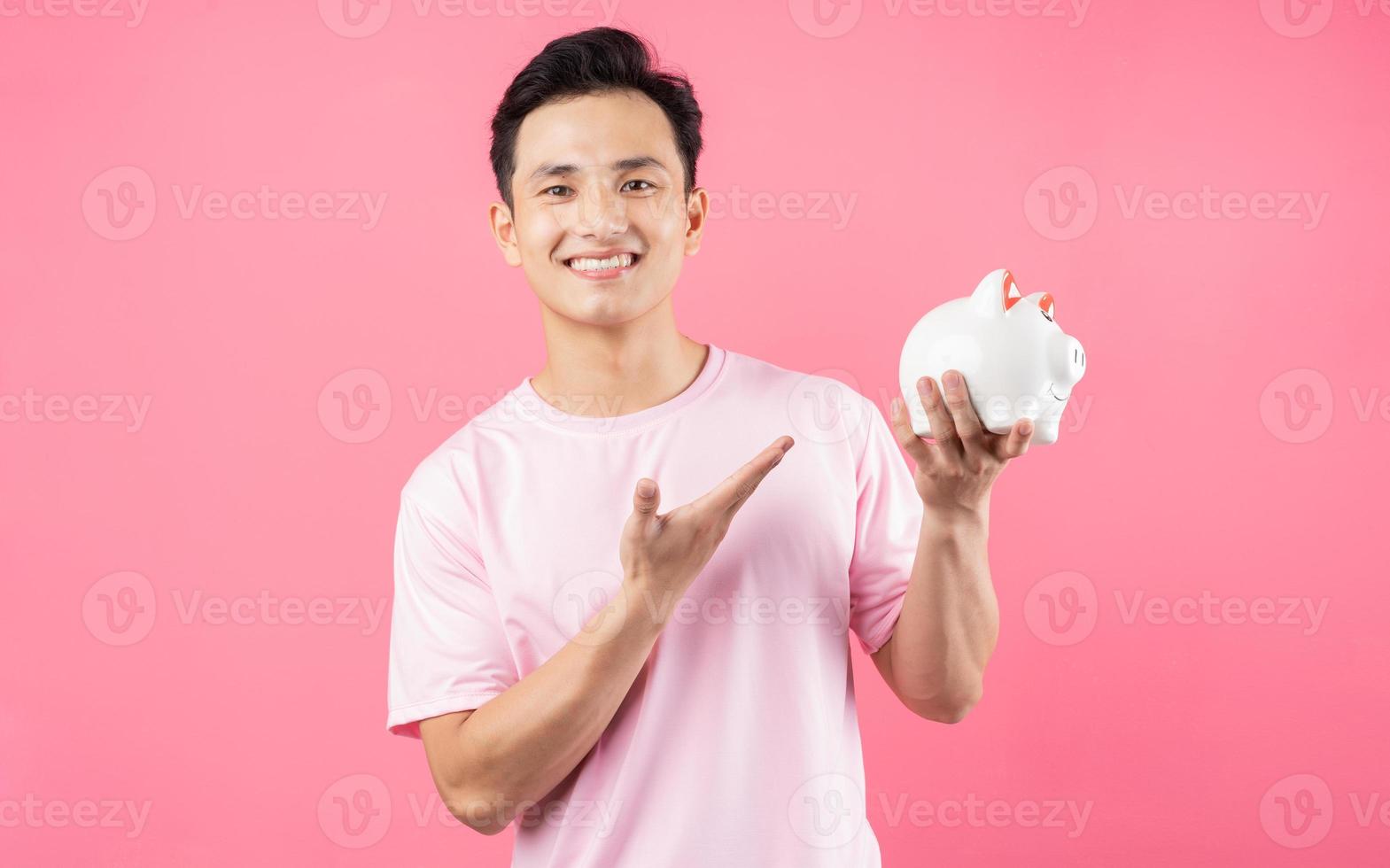 giovane uomo asiatico che tiene salvadanaio su sfondo rosa foto