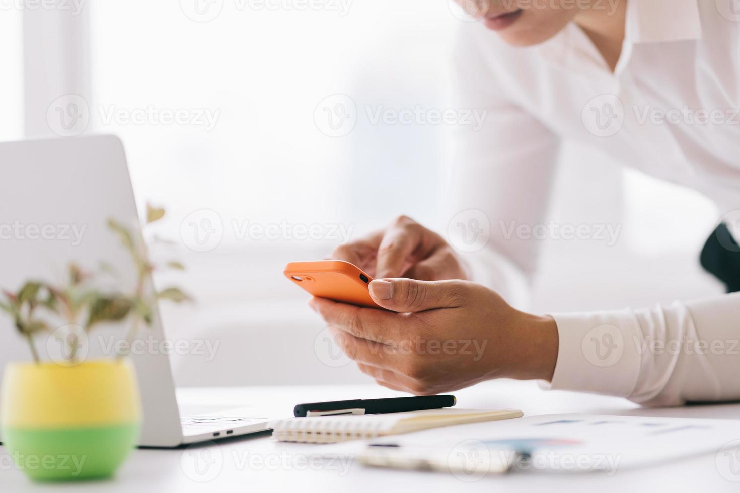 giovane uomo d'affari asiatico che utilizza smartphone e laptop in ufficio foto