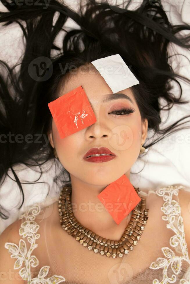 un asiatico donna con un' oro collana cascate addormentato con un' preservativo involucro su sua viso nel un' Hotel foto