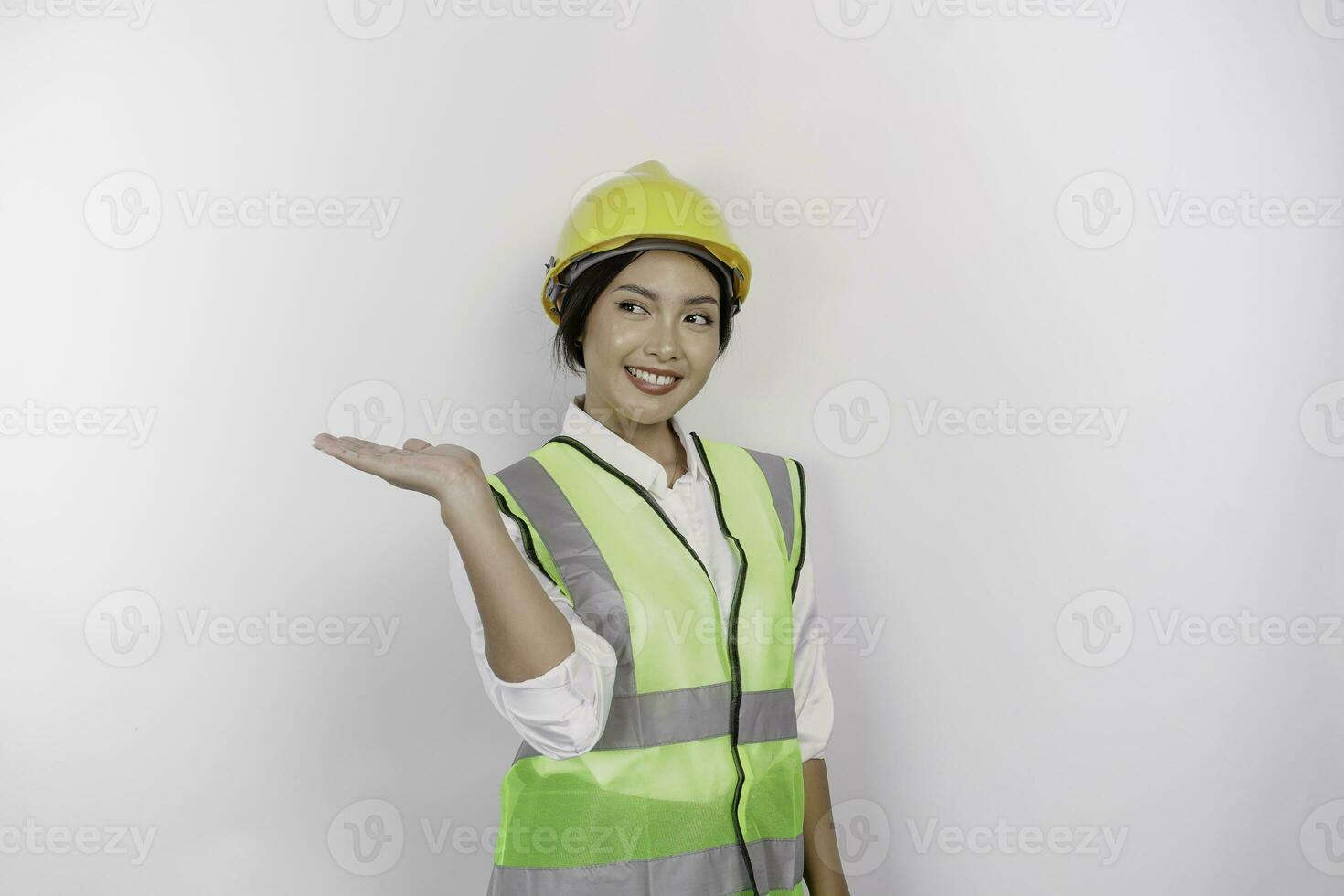 un' sorridente asiatico donna lavoro duro e faticoso indossare sicurezza casco e veste, puntamento per copia spazio accanto suo, isolato di bianca sfondo. lavoro giorno concetto. foto