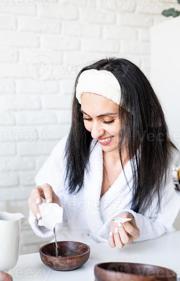 giovane donna sorridente felice in asciugamani da bagno bianchi che fanno maschera facciale facendo procedure termali foto