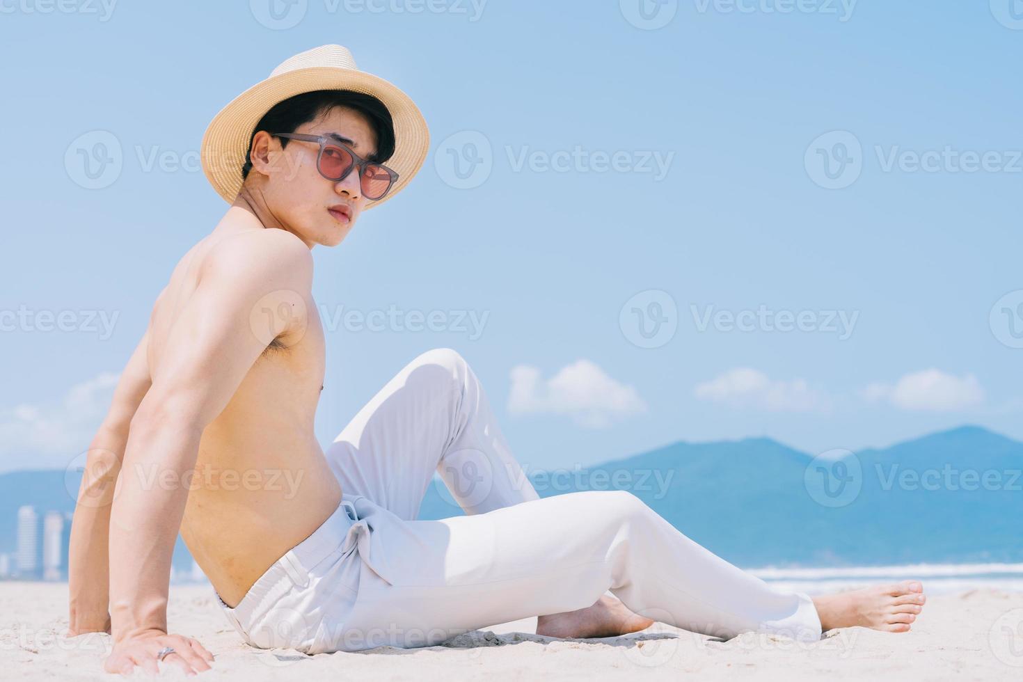 giovane asiatico senza sella seduto sulla sabbia e guardando il mare foto