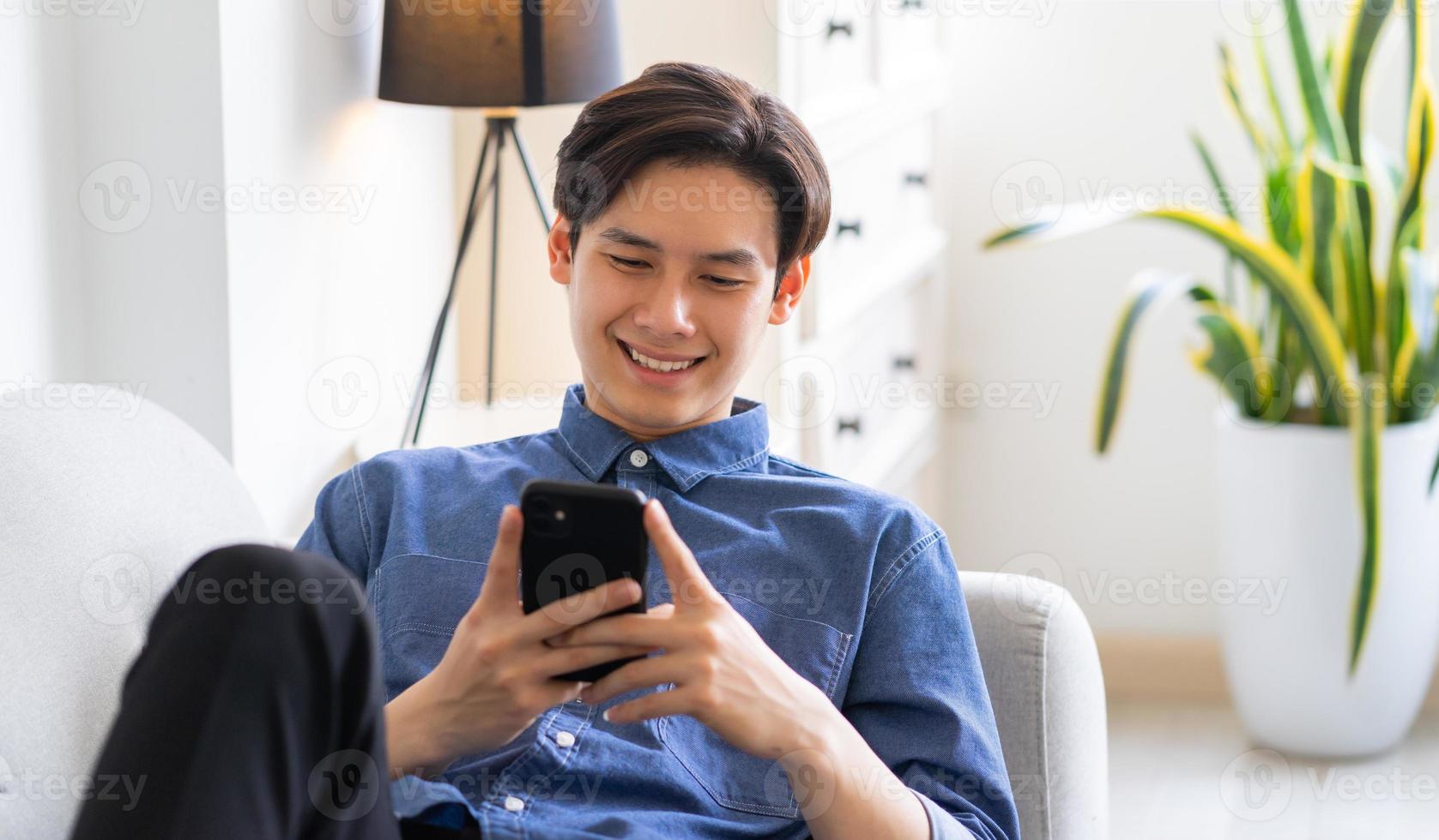 giovane uomo asiatico sdraiato sul divano e usando il telefono foto