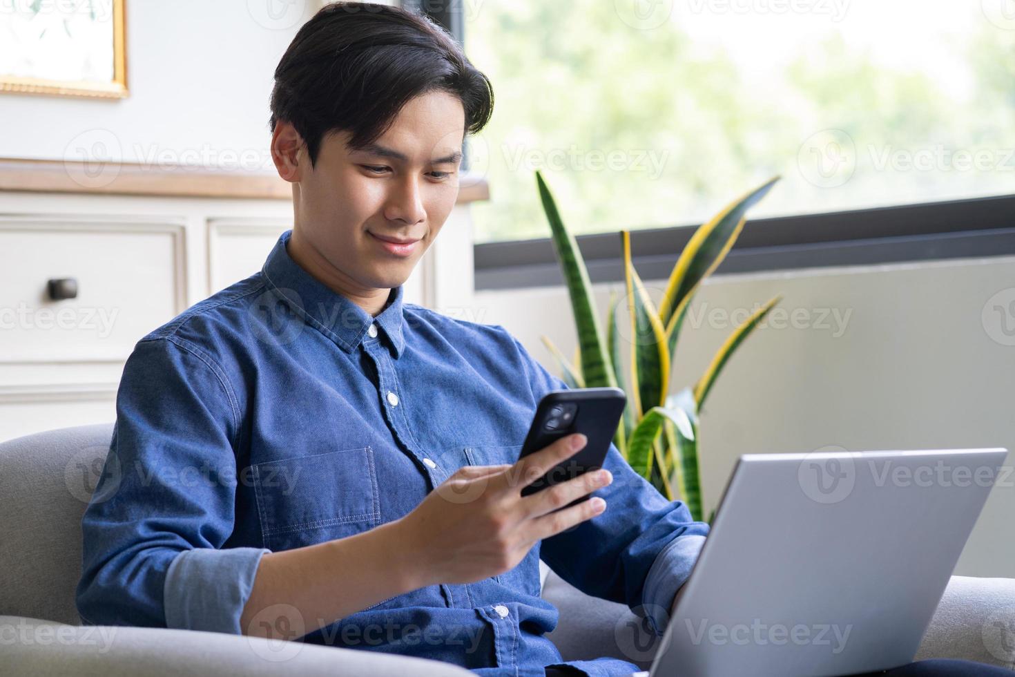 il giovane asiatico sta usando il telefono mentre usa il computer foto